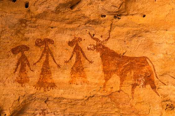 Prehistoric rock painting of three women wearing elaborate dresses and hats beside a cow, Terkei West, Ennedi Mountains, northeastern Chad