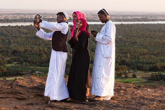 Local people on top of Jebel Barkal taking selfies at sunset, Karima, Northern Sudan