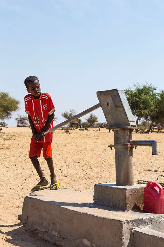 A boy pumping water at a well