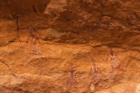 Rock painting depicting four women infilled, with the arms outstretched down. All the figures have white dots and lines throughout the body (garments), Kozen rock art site, Tibesti region