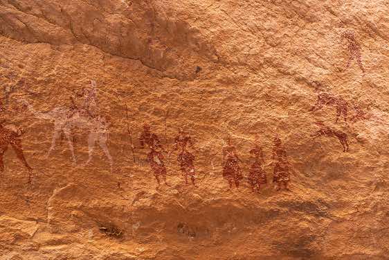 Rock painting depicting a rider on a camel, human figures and a hunting scene (upper right) with a human figure, two dogs chasing a goat, Kozen rock art site, Tibesti region
