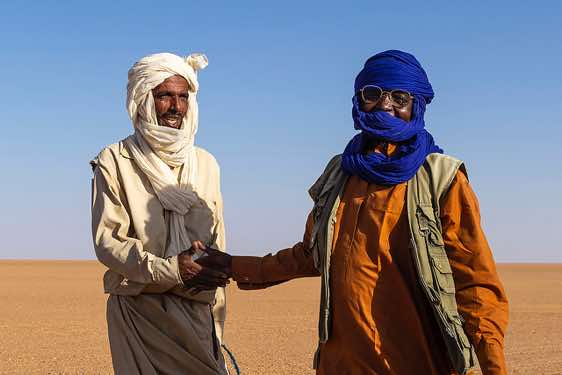 Camel herder (left) receives a gift of tea and sugar from our local guide and driver Omar