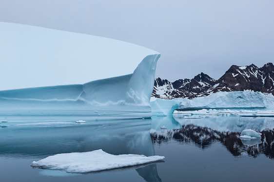 Iceberg and mountains reflecting in water, Ammassalik Island