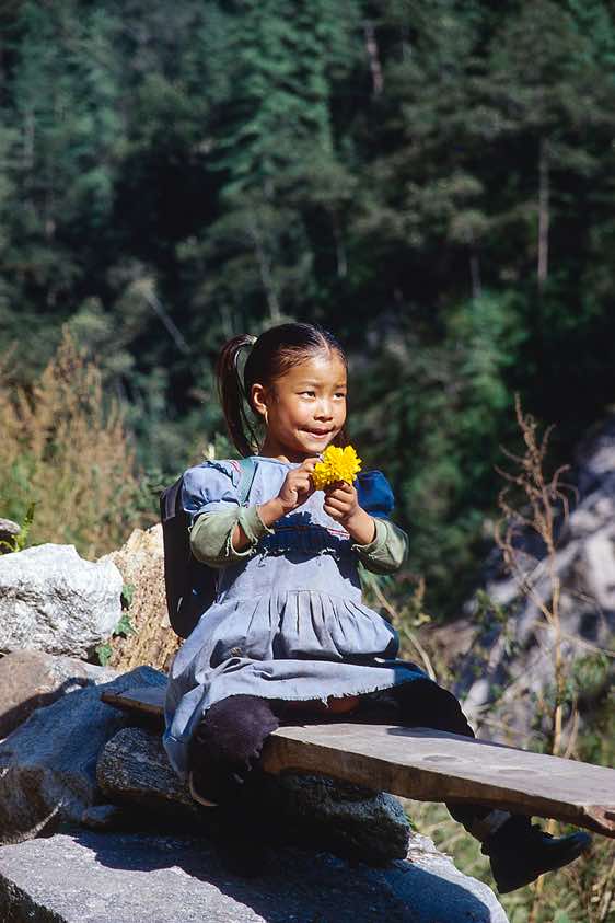A schoolgirl is watching the flow of trekking tourists