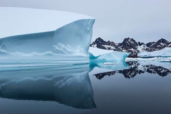 Iceberg and mountains reflecting in water, Ammassalik Island, East Greenland