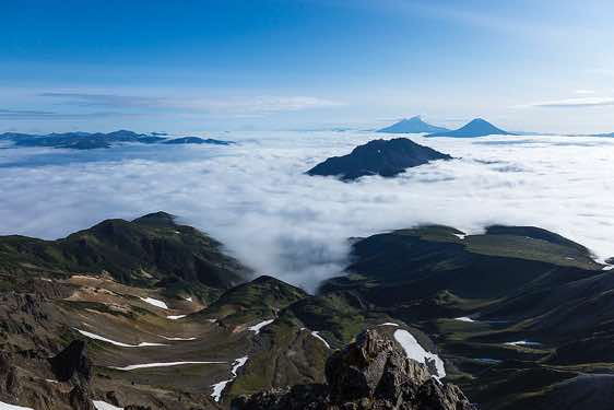 The cones of the Zheltovsky and Ilyinsky volcanos (background, from left) protrude from the sea of clouds, Pauzhetka area