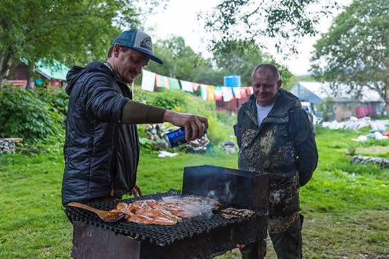 Russian guide Ivan prepares self-caught wild salmon on the grill. Driver Gena watches him with interest, Pauzhetka village