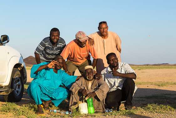 A nomad surrounded by our crew: Local guide Mohamed, driver Hawari, driver Abd Al Nasir (top), cook Moussa and driver Mudschahid, Bayuda Desert, Northern Sudan